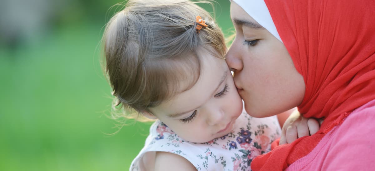 Mother with head covering kissing her young daughter